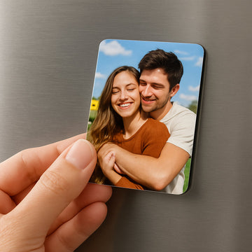 A close‑up of a hand holding a soft laminated mini photo magnet on a stainless‑steel fridge, showing the glossy finish and vibrant printed image. Alt: Mini photo magnets on a fridge surface showcasing material texture and color.